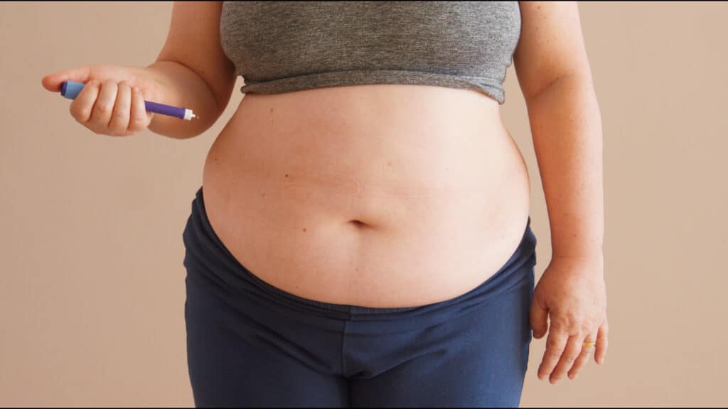 Overweight woman holding a diabetes medicine injection to apply in her belly